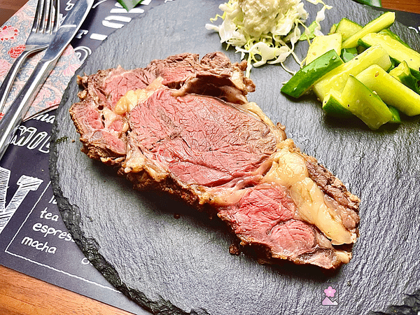 Close up of boneless ribeye slice on a slate plate. Cucumber and potato salad are also on the plate behind the roast.