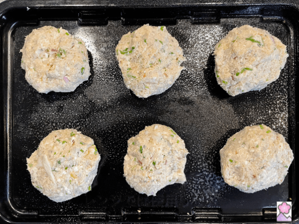 Six shellfish cakes before cooking on a baking pan