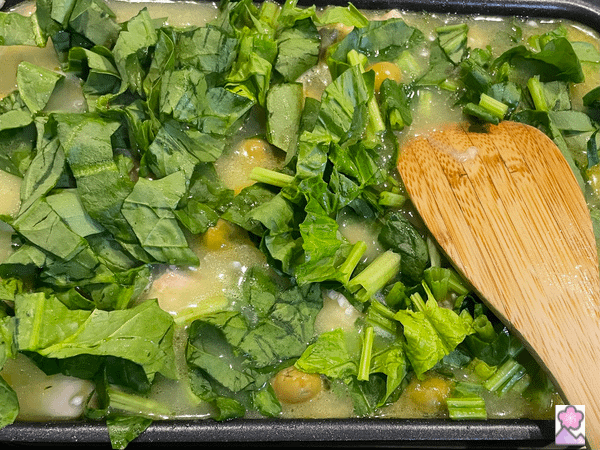 Pressing the greens into the consommé with a wooden spoon