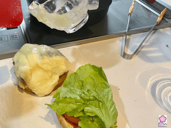 Preparing a burger. One half has a burger and cheese on it, the other is topped with lettuce and tomato.