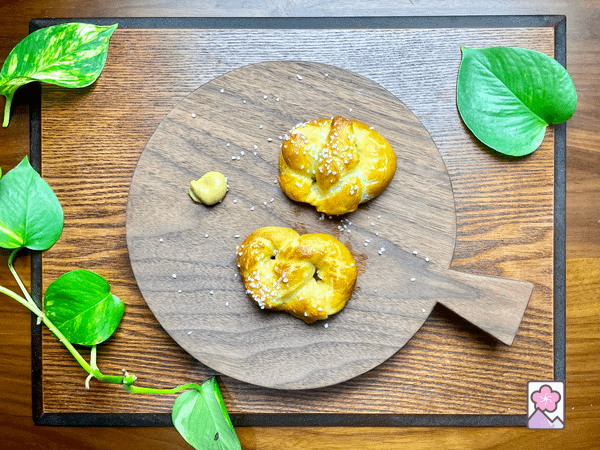 Two soft pretzels on a board with mustard.