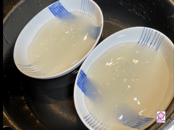 Kuzumochi in two shallow bowls sitting in a pan of water