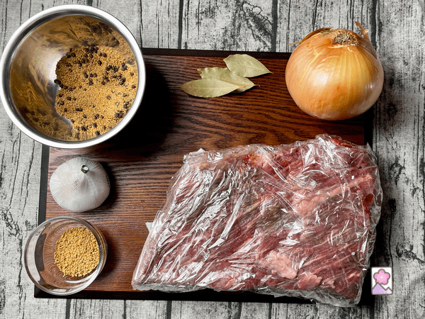 Irish corned beef ingredients on a board including a 5 lb brisket, garlic, onion, bay leaves, consommé crystals and mixed spices