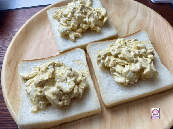 Spreading egg salad across three pieces of bread
