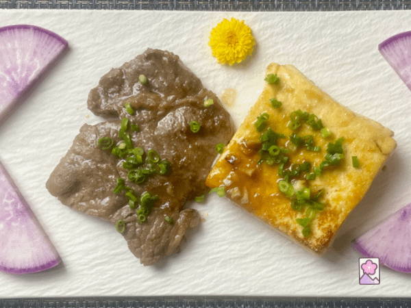 Wagyu and Tofu Stak in Japanese Fish Sauce on a ceramic plate with sliced radish and a chrysanthemum flower on the plate