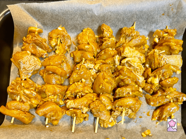 Six skewers of marinated chicken in a baking pan on parchment paper