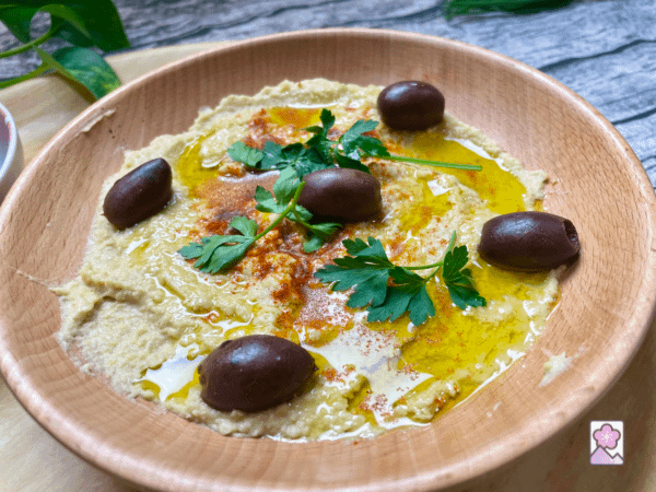 Hummus in a wood bowl ready to eat. Topped with paprika, olive,oil and black olives