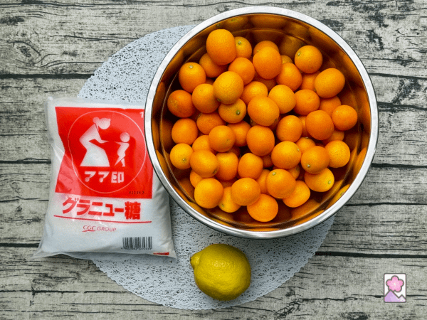 Poached Kinkan ingredients on a circular lace placemat. Kinkans, a lemon and a bag of granulated sugar