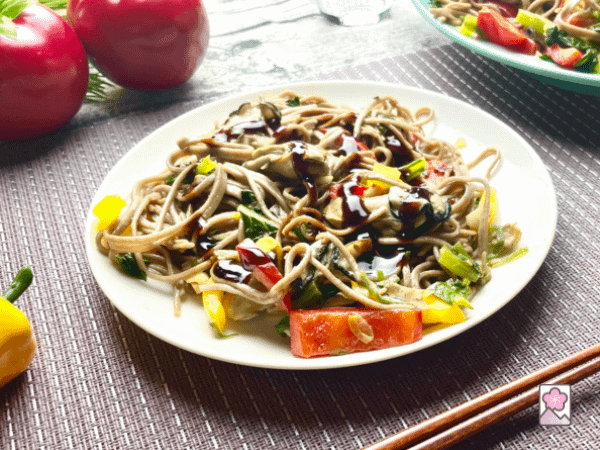Spicy Oyster Yakisoba on a plate with chopsticks and some veggies scattered around. It’s topped with yakisoba sauce.