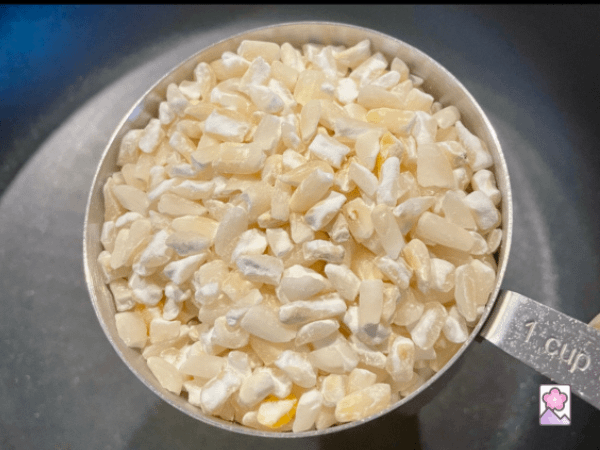 A cup full of dry hominy grains in a metal measuring cup