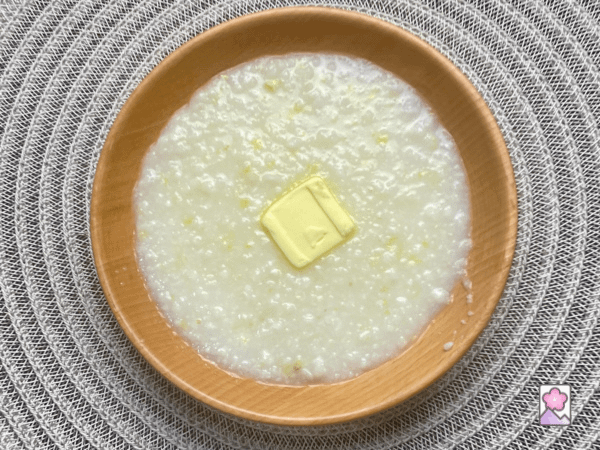 A wooden bowl of hominy grits with a butter patty melting on top