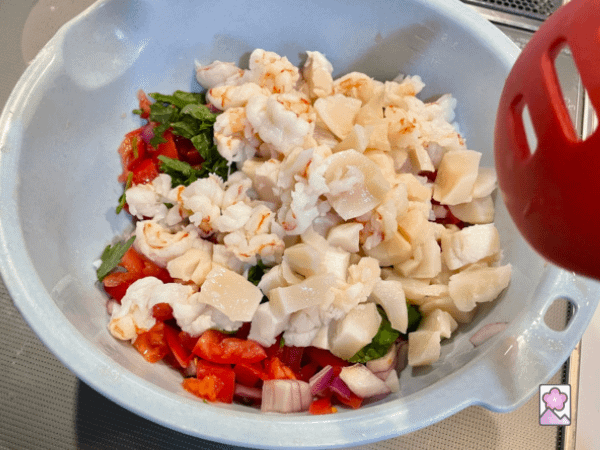 The seafood is added to the veggies and herbs in a large plastic bowl