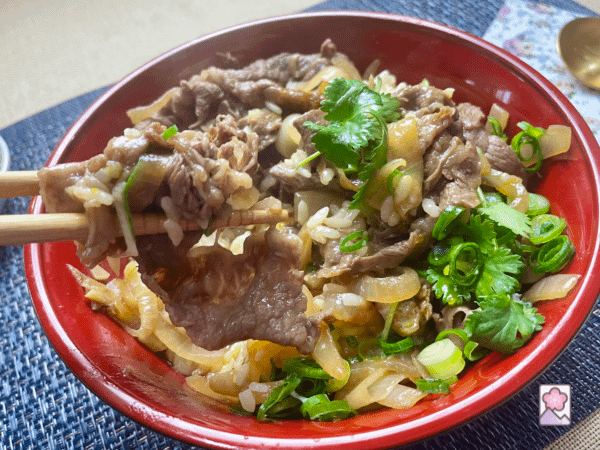 Picking up a piece of beef from the rice bowl with chopsticks
