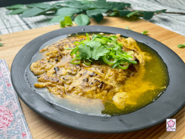 Roast Pork Egg Foo Young on a plate covered with gravy and garnished with scallions and corriander
