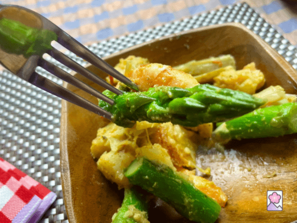 A fork with a piece of shrimp and asparagus is lifted from a wooden bowl full of Roasted Seafood and Asparagus Salad