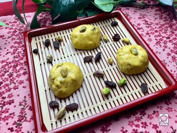 Three laddu on a square plate with a cooling grid fitted in. It all on a flowered tablecloth