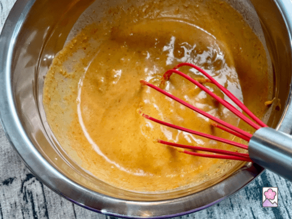 Whisking peanut sauce in a metal bowl with a wire whisk