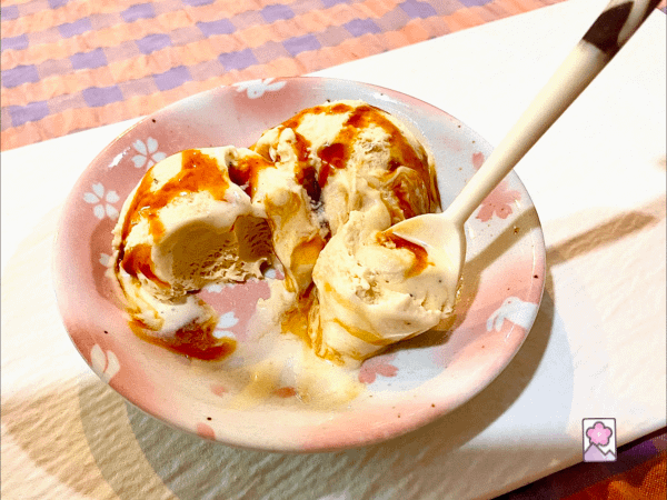A plate of Rich Creamy Caramel Ice Cream topped with caramel. A spoonful of ice cream is being held up.