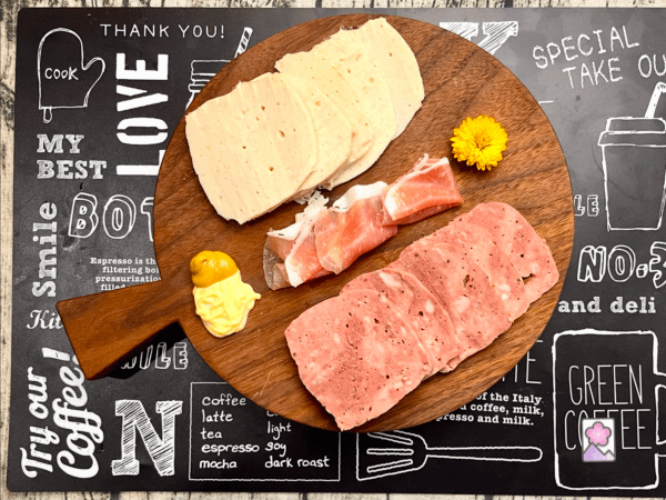 Charcuterie board featuring homemade bologna, chicken roll, and prosciutto ham