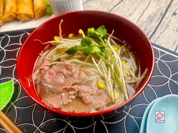 Vietnamese Pho Noodle Soup served in a bowl with egg rolls on the side
