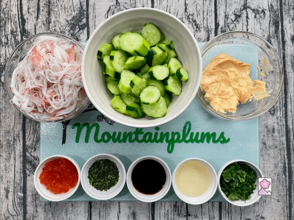 Kani Salad with Mentaiko Dressing ingredients are lined up on a glass mountain plums cutting board