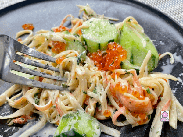 A forkful of Kani Salad with Mentaiko Dressing loaded with seafood salad, cucumber slices, and Ikura (Salmon Roe)