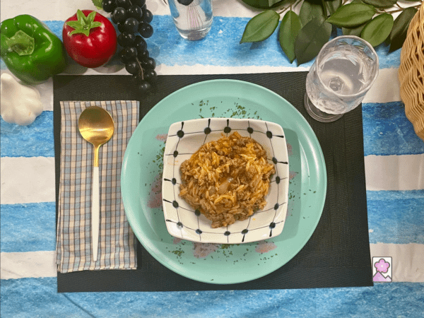 Youvetsi is served in a square bowl with a glass of flavored water and a golden spoon