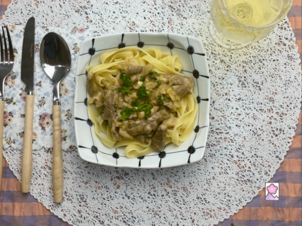 Wagyu Stroganoff over pasta in a squared ceramic bowl