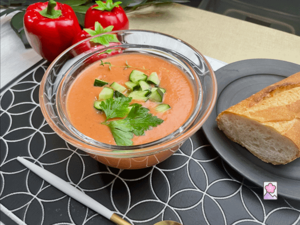 Chilled Gazpacho served in a glass bowl with chopped cucumbers and fresh herbs
