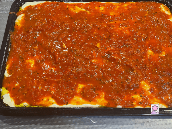 The pizza sauce is spread across the dough as the pizza takes shape
