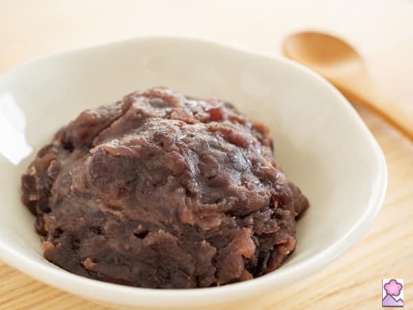 Japanese coarse bean paste in a white bowl sitting on a wood table. There is a wood spoon in the background.
