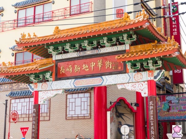 Four red pillars top-Ed with a sloped roof adorned with Chinese characters with a brick building in the background.