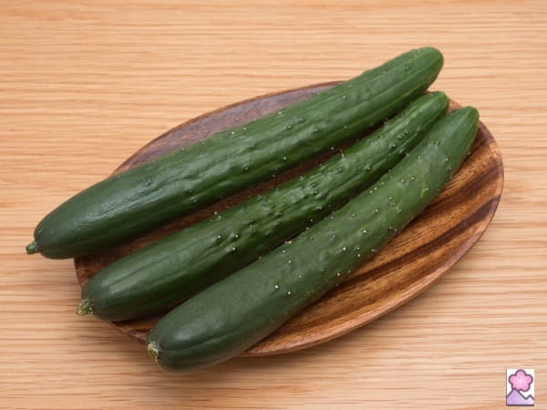 Three Japanese cucumbers on a wood plate sitting on a wooden tabletop