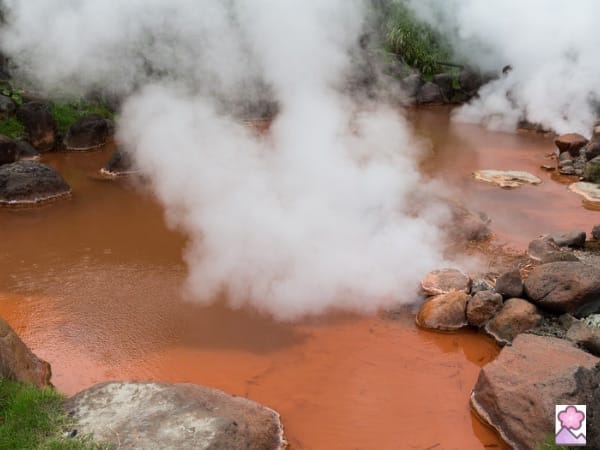 A blood red hot spring surrounded by rocks and smoking hot