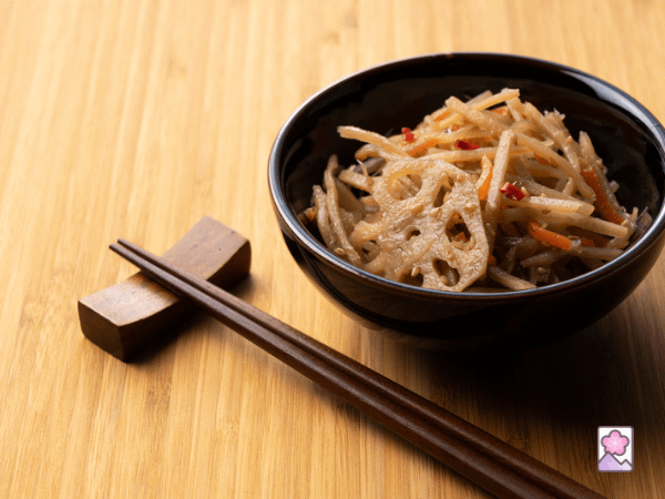 Kinpira gobo, julienne cut burdock root is mixed with carrot and lotus root and tossed in a small bowl. Wooden chopsticks are sitting nearby.
