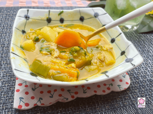 A golden spoon scoops some Kabocha soup out of a ceramic bowl