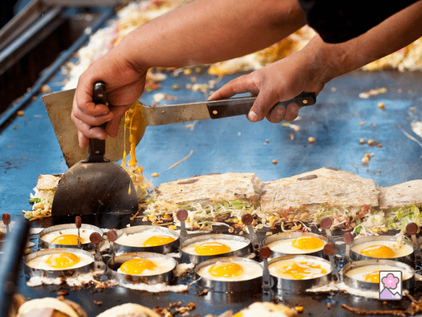 A chef cooks many okonomiyaki pancakes on a steam table