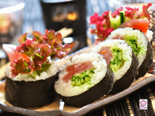 Futomaki, giant sushi rolls, stuffed with fish and lettuce surrounded by rice and nori, sitting on a ceramic tray